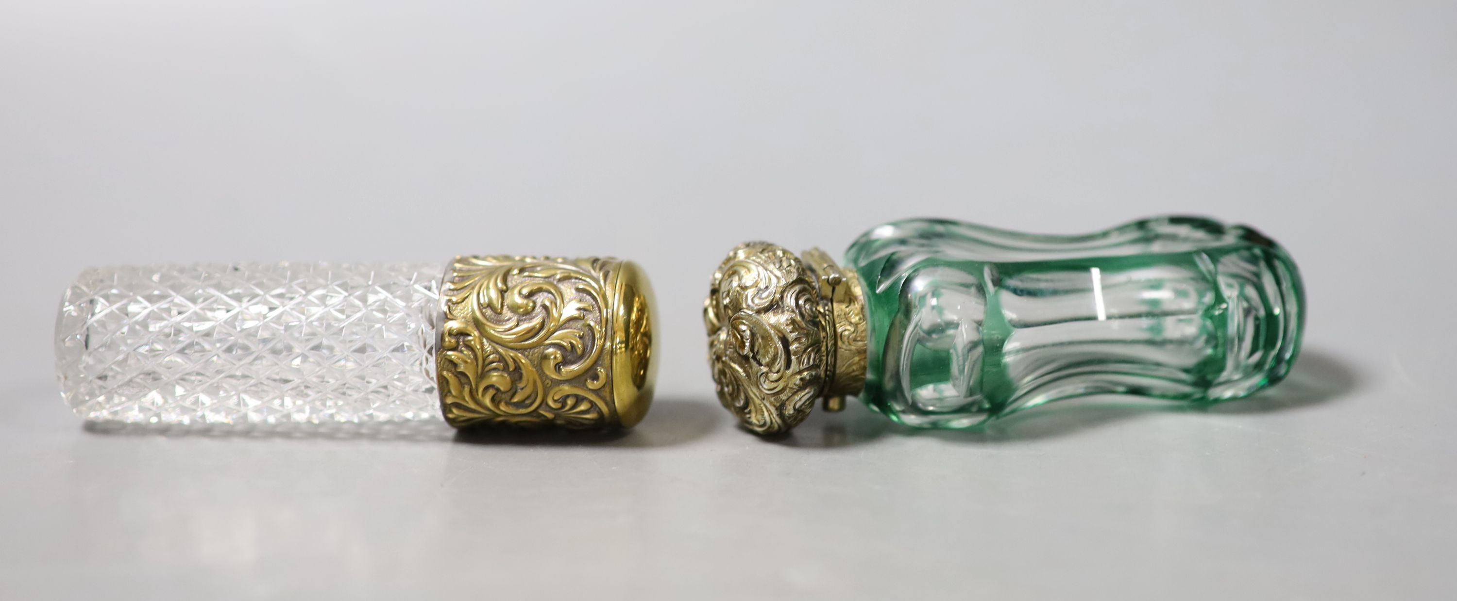 A late Victorian repousse gilt white metal mounted green and clear glass waisted scent bottle, 86mm and one other gilt metal mounted glass scent bottle.